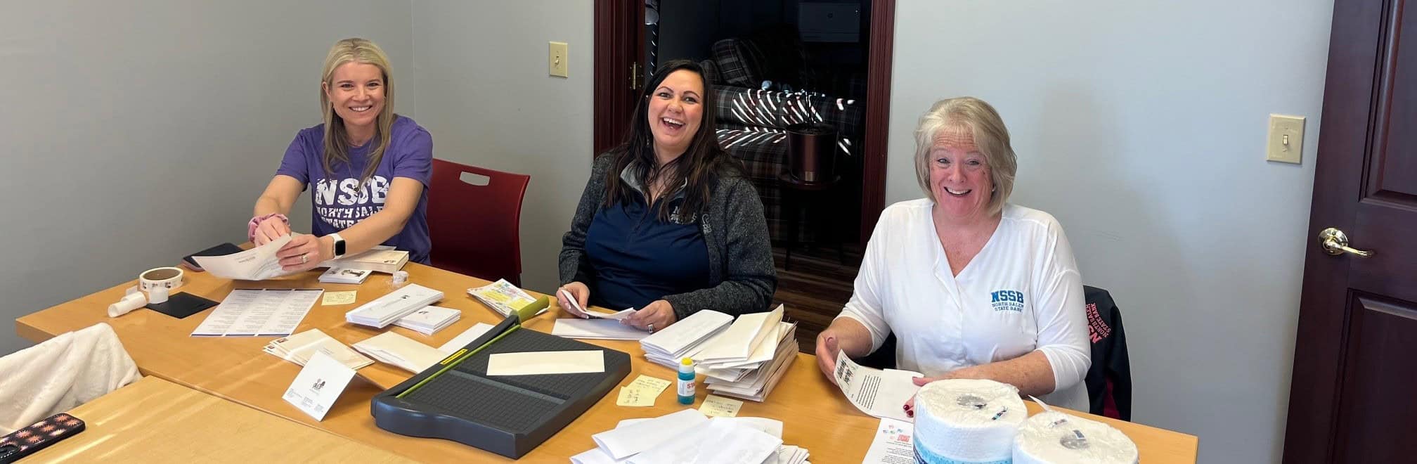 Volunteer with Susie's Place 1 Three Susie’s Place volunteers smiling while sorting mail and paperwork at a conference table